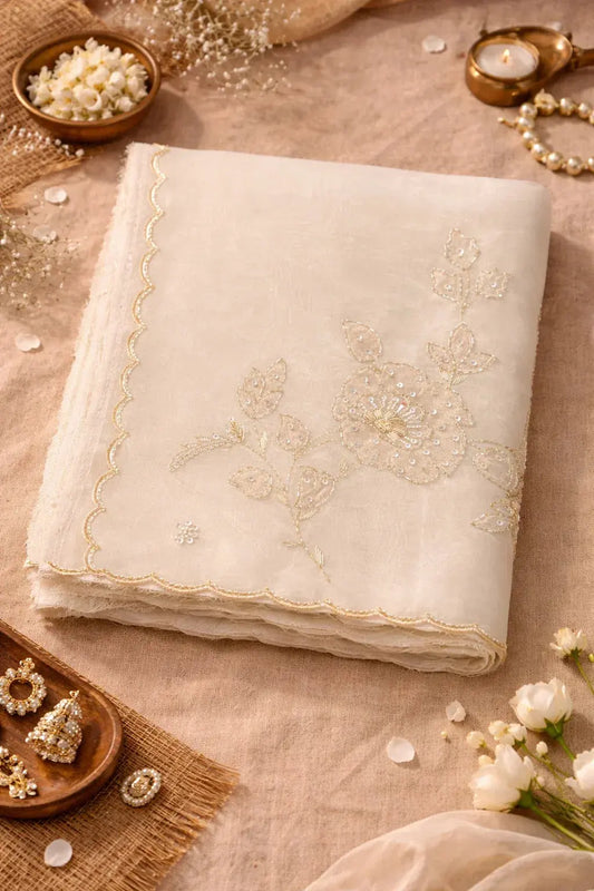 Folded soft silk saree with gold floral embroidery, surrounded by flowers and jewelry