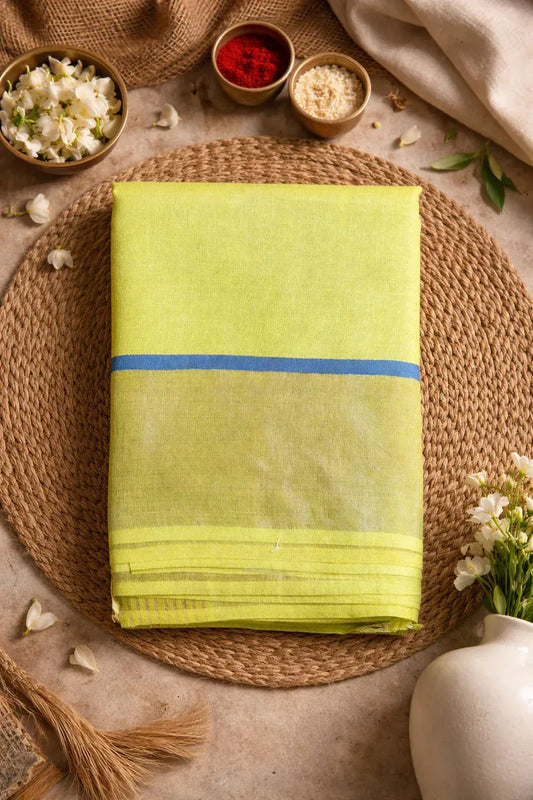 Folded yellow silk saree with blue border, displayed on a woven mat with flowers and decor
