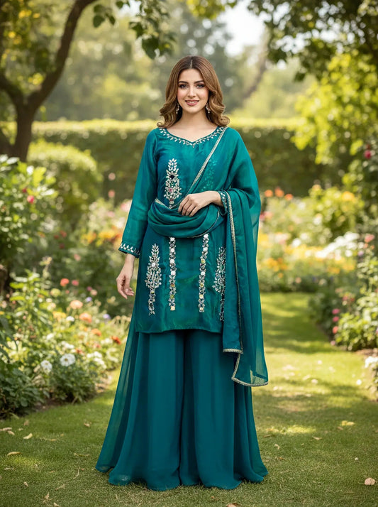 Woman in teal embroidered silk ethnic suit with dupatta standing in a garden