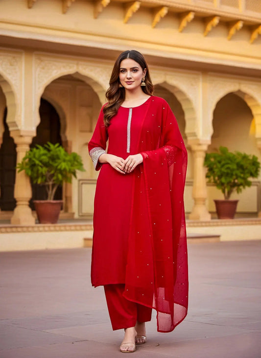Woman in red silk salwar suit with embellished details, standing in a traditional courtyard