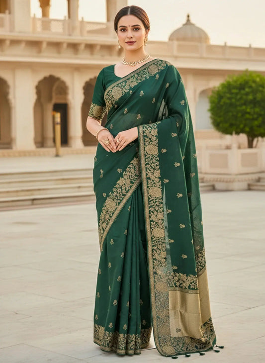 Woman in green soft silk saree with gold floral embroidery, standing in an elegant courtyard