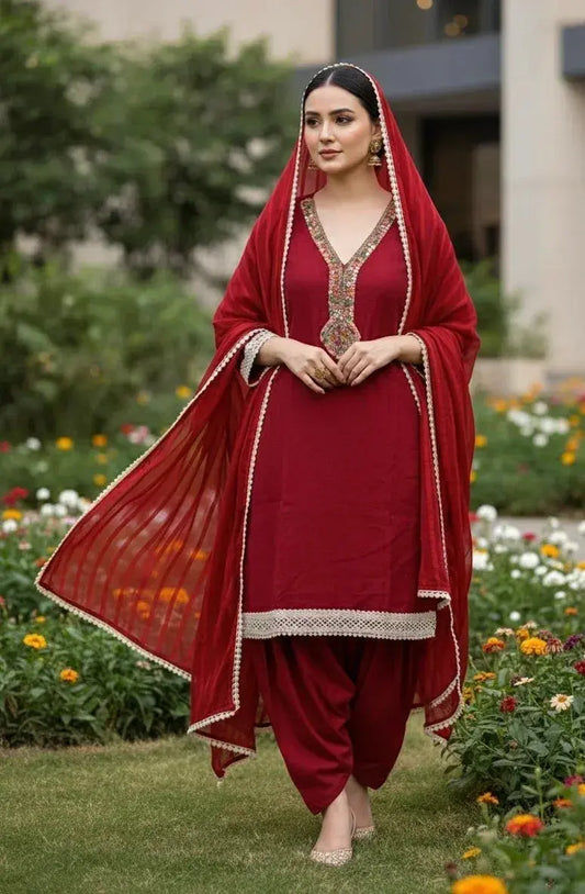 Woman in red embroidered ethnic suit and dupatta standing in a garden with flowers