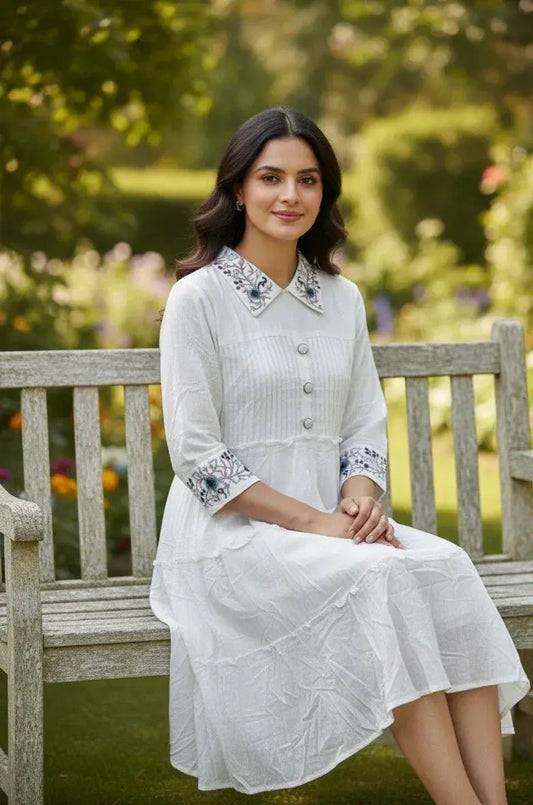 Woman in white embroidered dress sitting on wooden bench in a garden setting