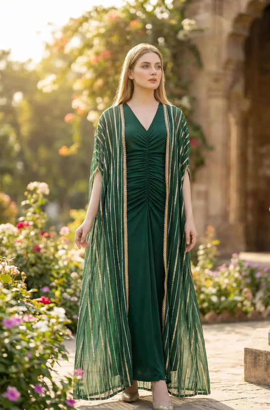 Woman in a green ethnic gown with gold stripes, posing outdoors near blooming flowers.