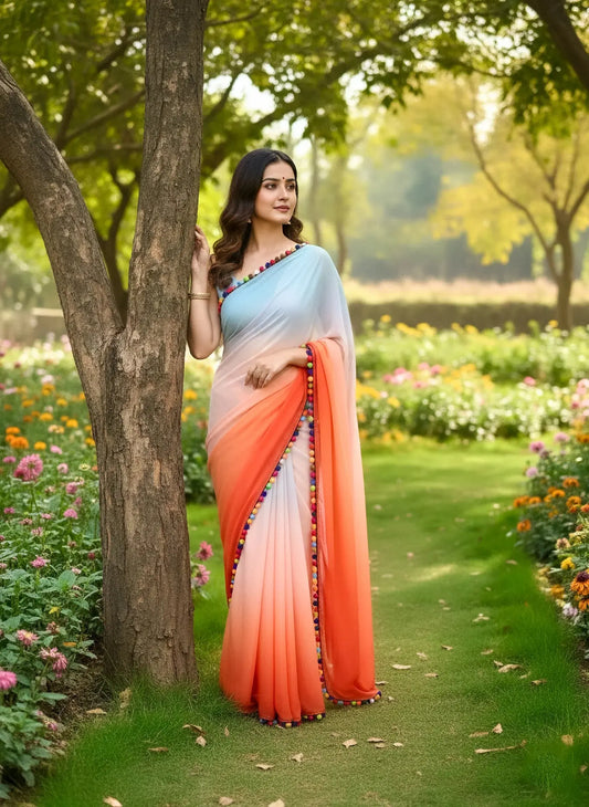 Woman in a pastel gradient soft silk saree with colorful border, standing in a lush garden with blooming flowers.