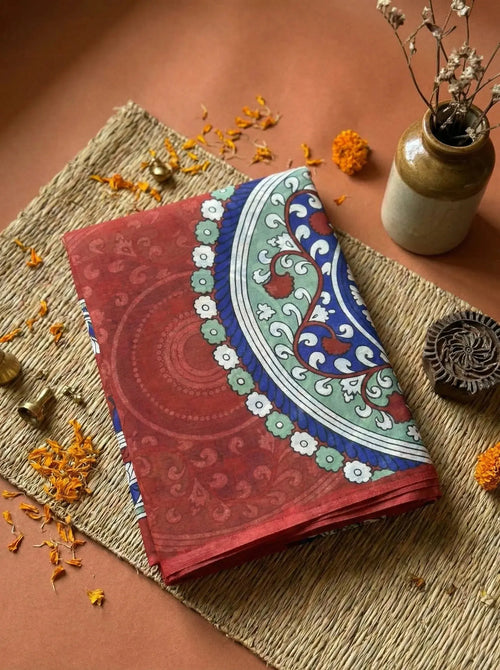 Soft silk saree with maroon and blue floral pattern, displayed on a woven mat with festive decor