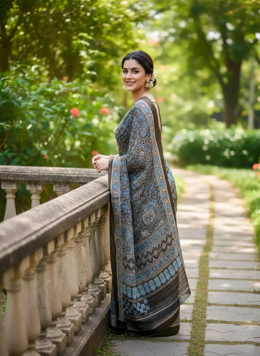 Woman in a soft silk saree with blue and black intricate patterns standing outdoors by a stone railing