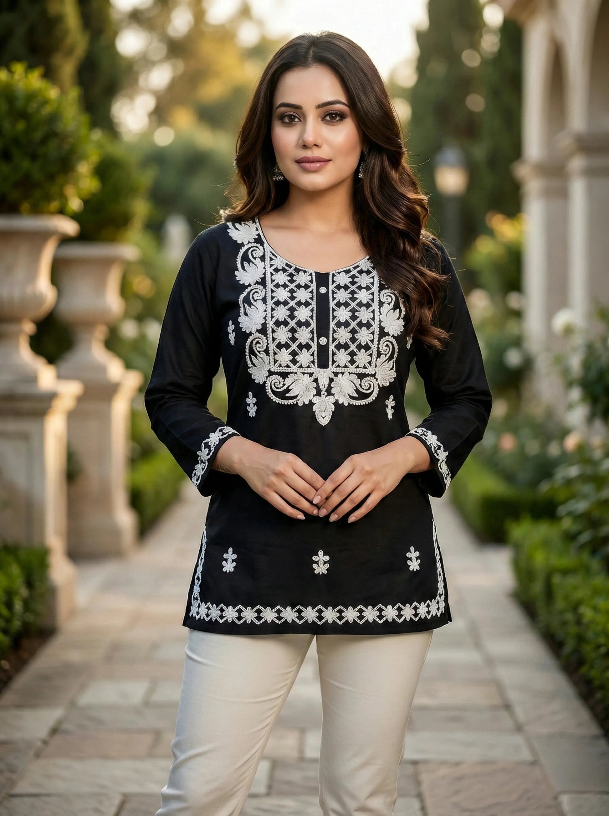 Woman in black and white embroidered kurta and cream pants, standing outdoors in garden