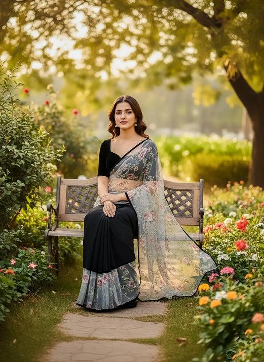 Woman in a black soft silk saree with floral print sitting on a bench in a flower garden