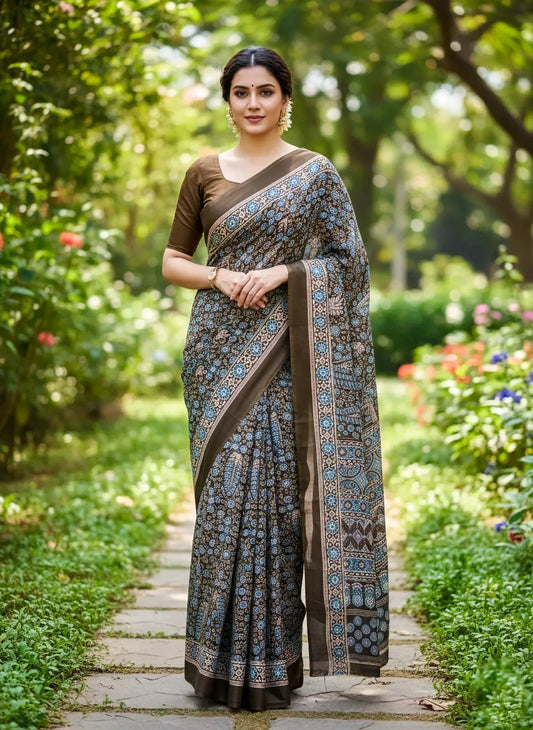 Woman in a blue and brown soft silk saree with floral patterns, standing outdoors in a garden