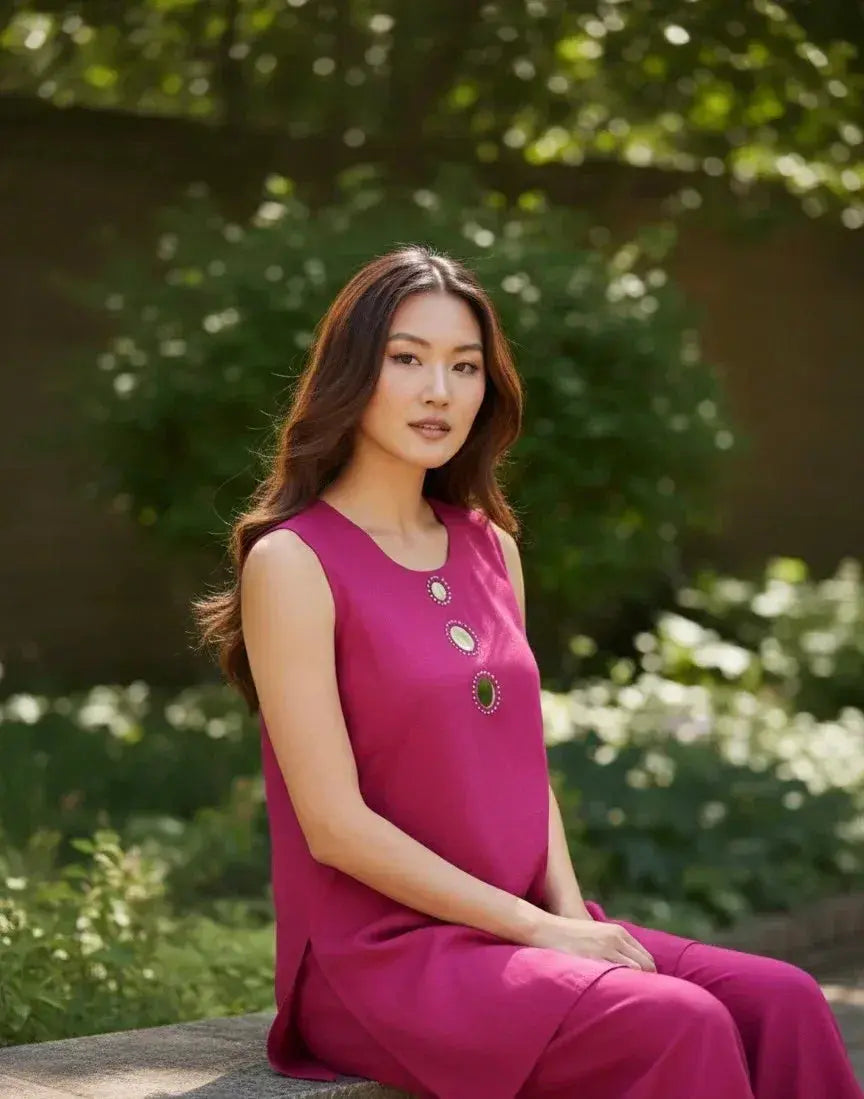 Woman in sleeveless magenta kurta set with stone embellishments, seated outdoors