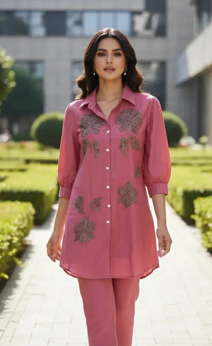 Woman in pink embroidered kurta with floral patterns, paired with matching trousers, outdoors