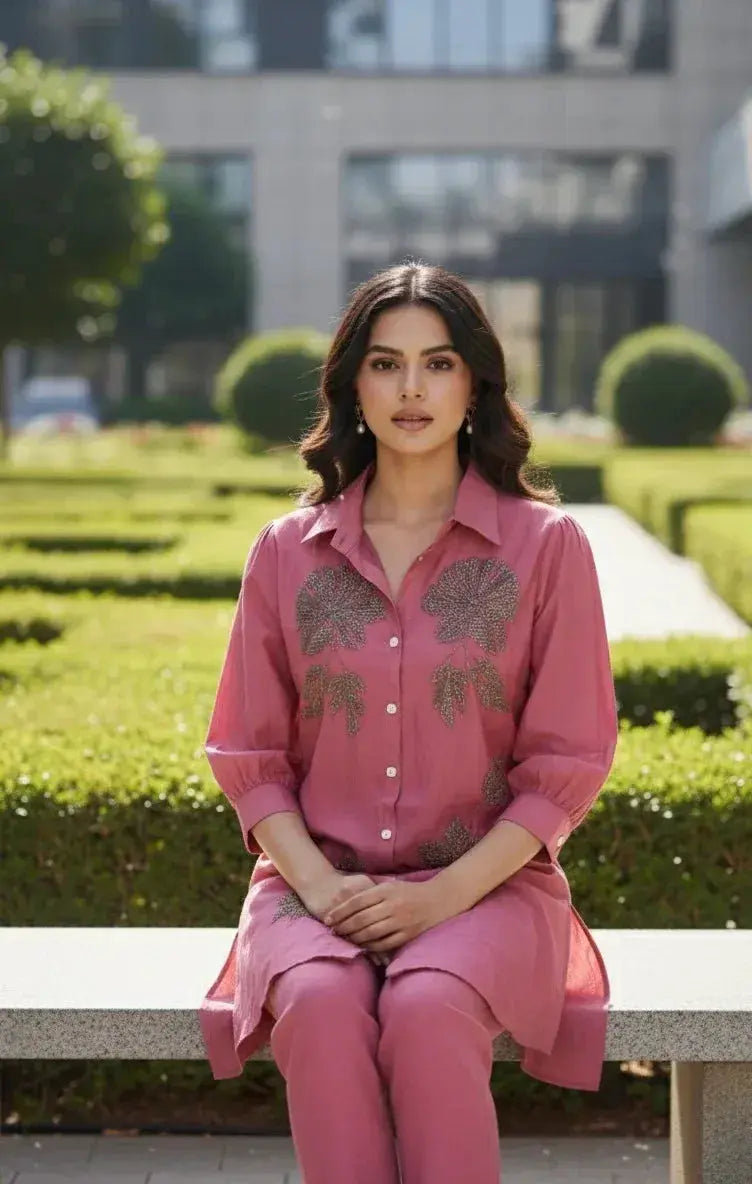 Woman in a pink embroidered kurta and pants sitting on a bench in a manicured garden
