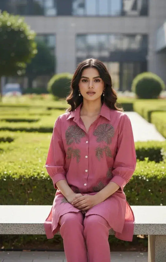 Woman in a pink embroidered kurta and pants sitting on a bench in a manicured garden