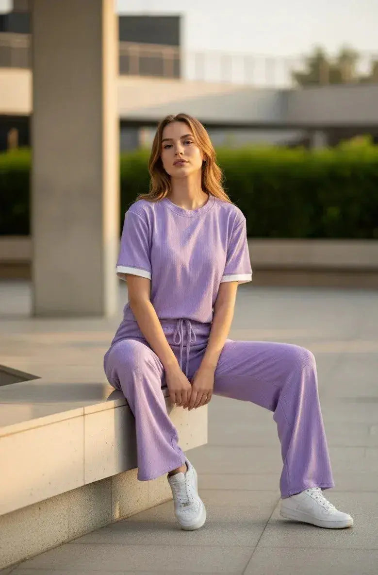 Woman in a lavender loungewear set with white sneakers, seated outdoors in modern setting