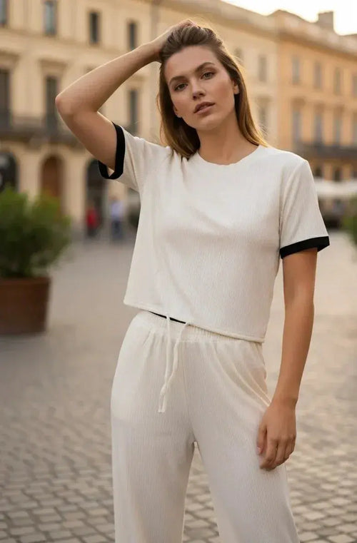 Woman in cream lounge set with drawstring pants and black trim, posing outdoors on a city street