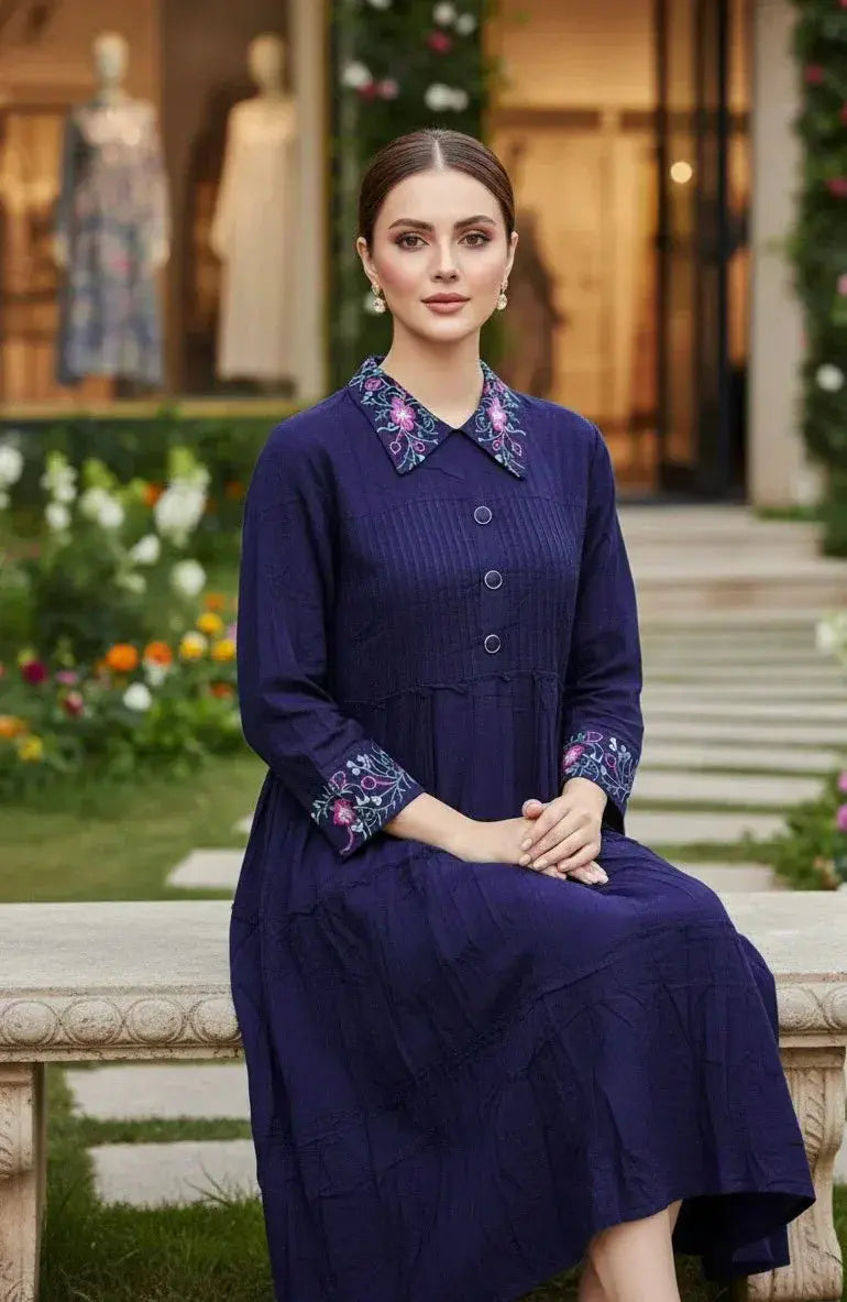Woman in a navy blue embroidered ethnic dress with floral collar, seated in a garden.