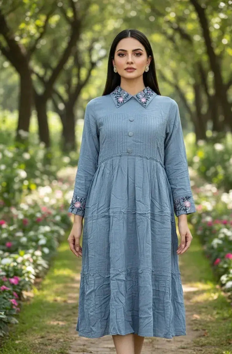 Woman modeling a blue cotton dress with embroidered collar and cuffs in a garden setting