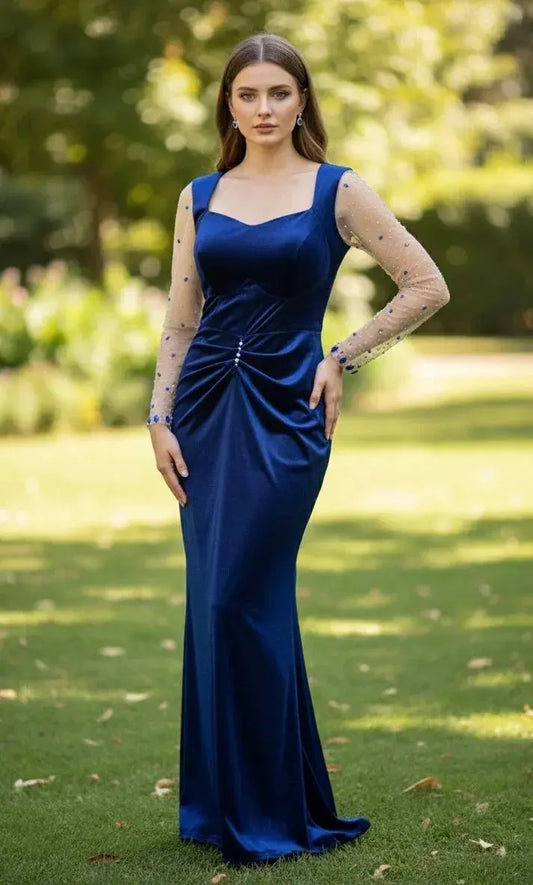 Woman in a blue velvet evening gown with sheer embellished sleeves, standing outdoors