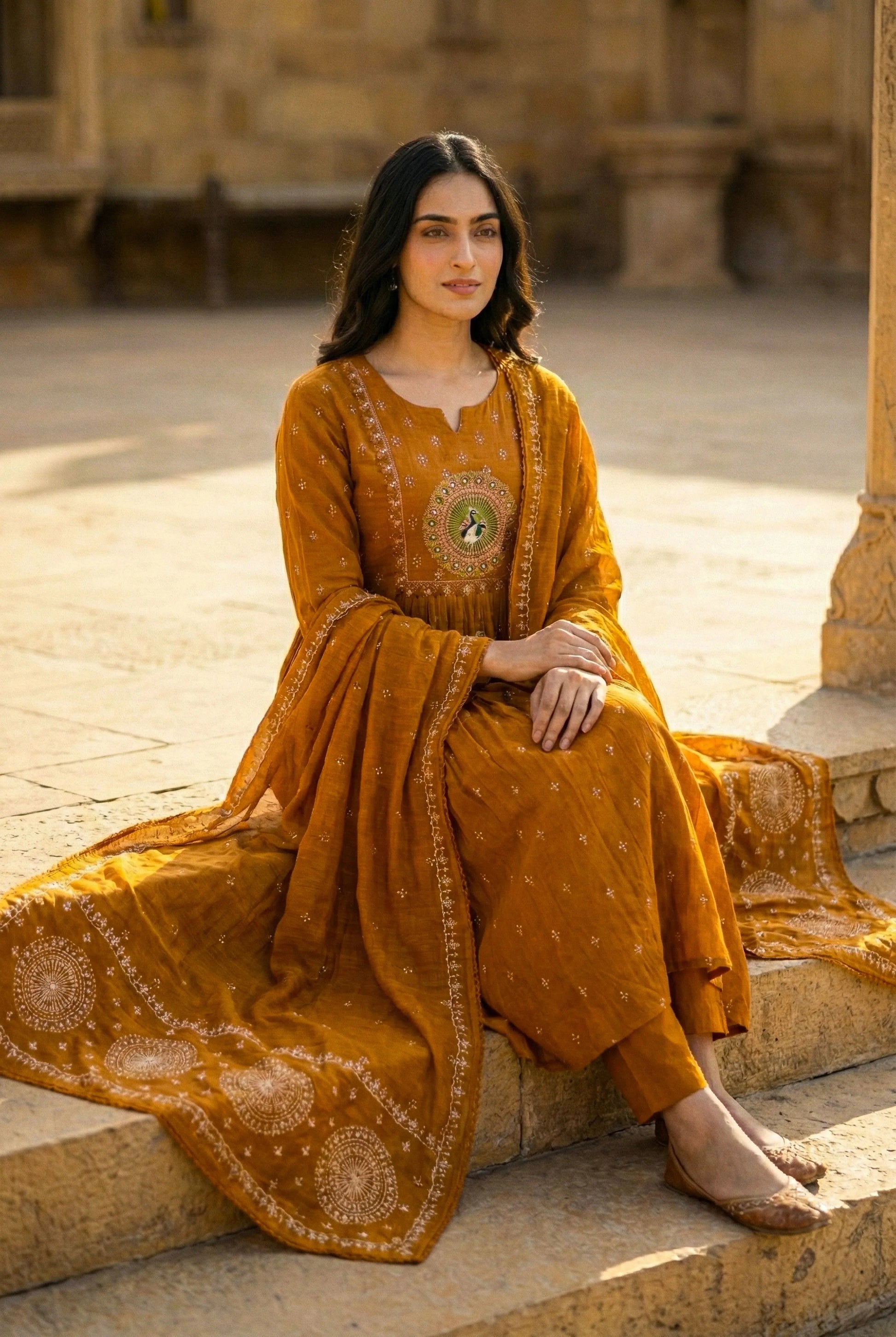 Woman wearing mustard yellow pure cotton ethnic 3-piece suit set with dupatta, sitting outdoors.