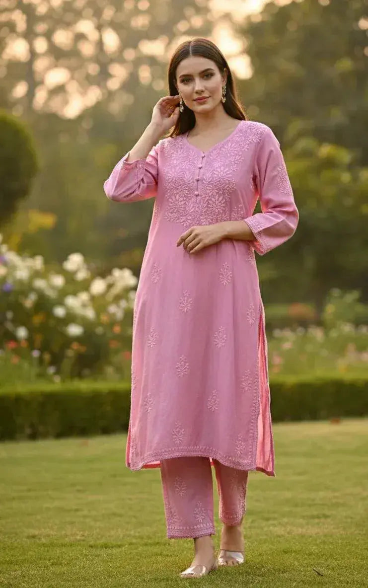 Woman in pink embroidered kurta set with straight pants, standing outdoors on grass