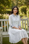Woman in white embroidered dress sitting on wooden bench in a garden setting