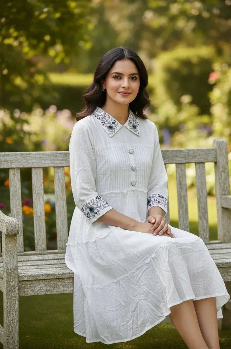 Woman in white embroidered dress sitting on wooden bench in a garden setting