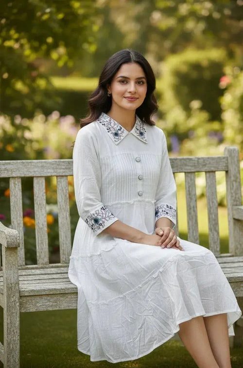 Woman in white embroidered dress sitting on wooden bench in a garden setting